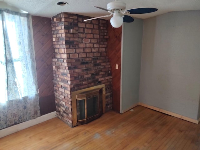 unfurnished living room featuring ceiling fan, wood walls, hardwood / wood-style floors, a textured ceiling, and a fireplace