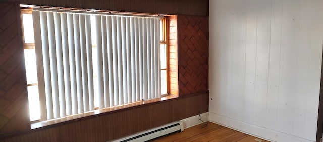 unfurnished room featuring hardwood / wood-style floors and a baseboard heating unit