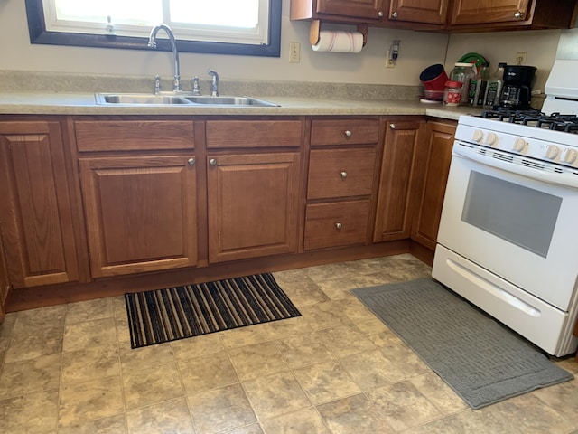 kitchen with brown cabinets, light countertops, a sink, and white gas stove