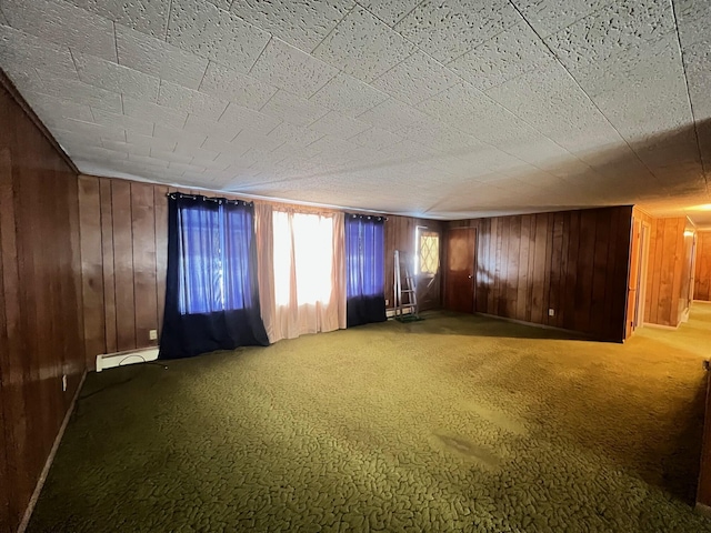 unfurnished room with carpet, a baseboard heating unit, and wood walls