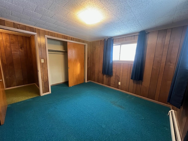 unfurnished bedroom featuring dark carpet, a closet, wooden walls, and a baseboard heating unit