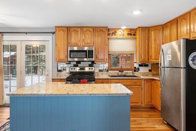 kitchen with sink, a center island, stainless steel appliances, light stone countertops, and light wood-type flooring