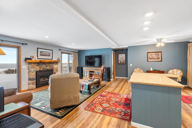 living room with a stone fireplace, ceiling fan, and light wood-type flooring