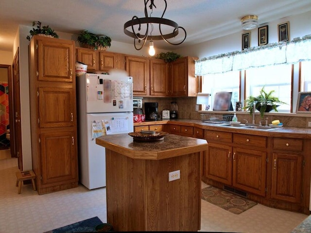 kitchen featuring tasteful backsplash, sink, white refrigerator, decorative light fixtures, and a center island