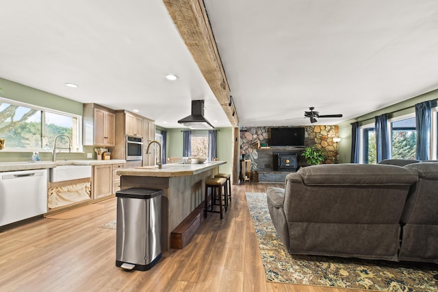 kitchen with wall chimney exhaust hood, dishwashing machine, a fireplace, oven, and an island with sink