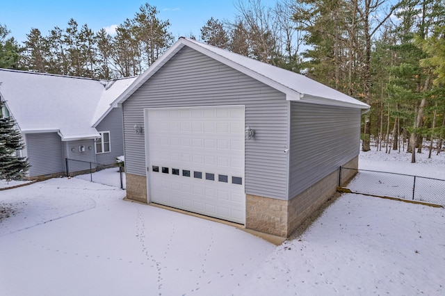 snow covered garage with a garage and fence