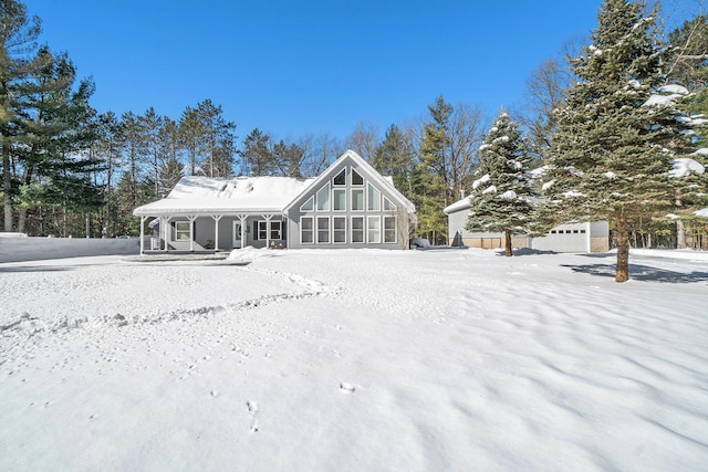 snow covered back of property with a garage, a porch, and an outdoor structure