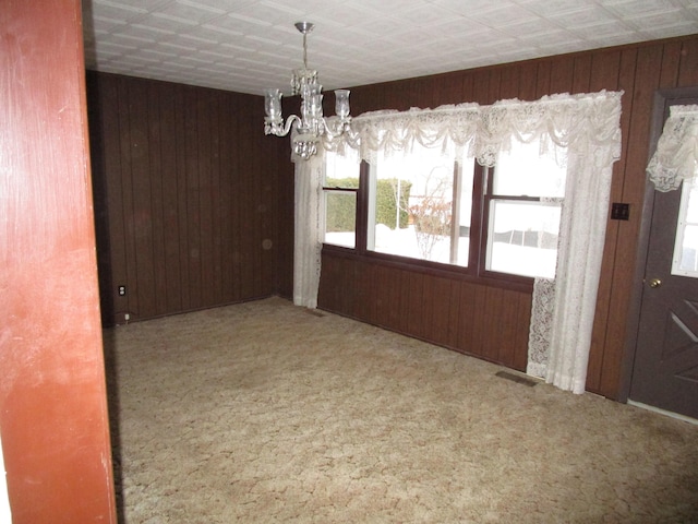 unfurnished dining area with carpet flooring, an inviting chandelier, plenty of natural light, and wooden walls