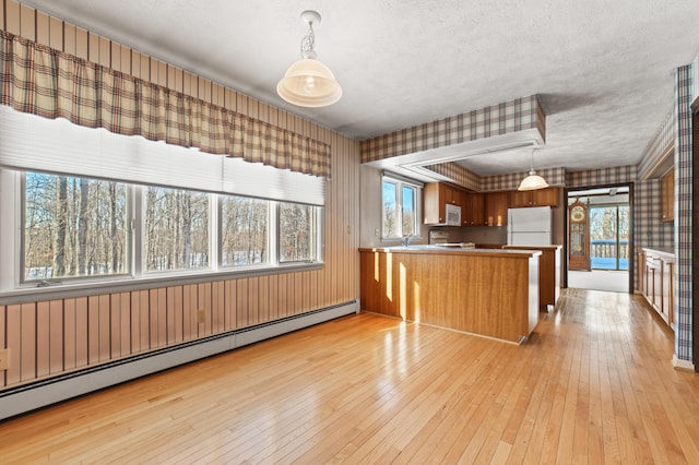 kitchen with white appliances, hanging light fixtures, baseboard heating, light hardwood / wood-style floors, and kitchen peninsula