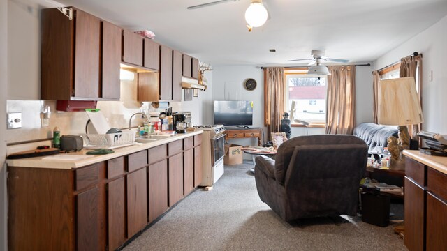 kitchen with white range with gas stovetop, light carpet, ceiling fan, and sink