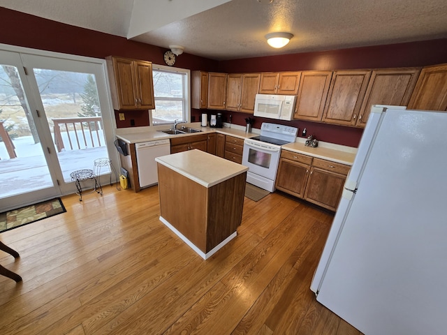 kitchen with a textured ceiling, white appliances, a center island, and sink