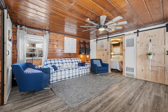 living room with wood-type flooring, wooden walls, ceiling fan, wooden ceiling, and a barn door