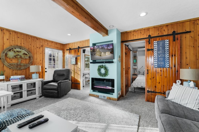 living room featuring light carpet, beam ceiling, a barn door, and wooden walls