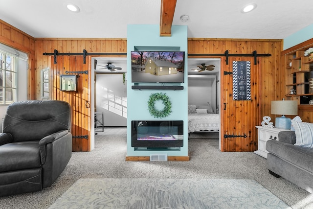 carpeted living room with ceiling fan, beam ceiling, and wood walls