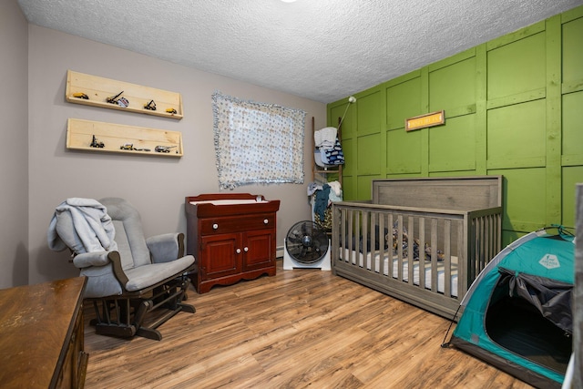 bedroom with a crib, a textured ceiling, a baseboard radiator, and light hardwood / wood-style flooring