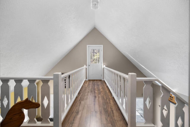 hallway with a textured ceiling, vaulted ceiling, and dark wood-type flooring