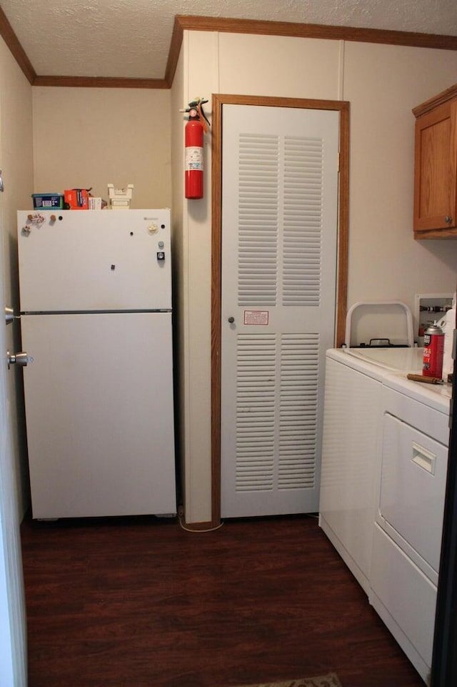 washroom featuring washing machine and clothes dryer, cabinets, dark hardwood / wood-style flooring, a textured ceiling, and ornamental molding