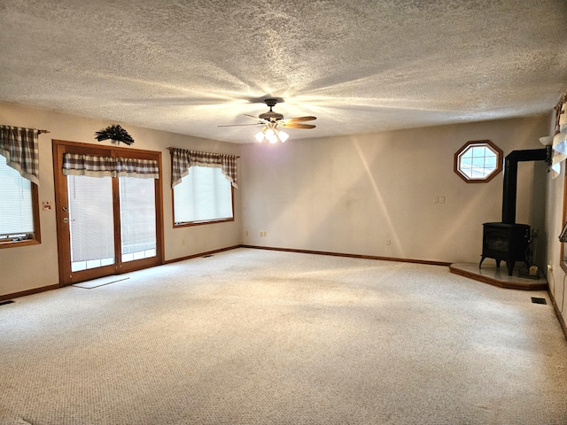 unfurnished living room featuring ceiling fan, carpet, a wealth of natural light, and a wood stove