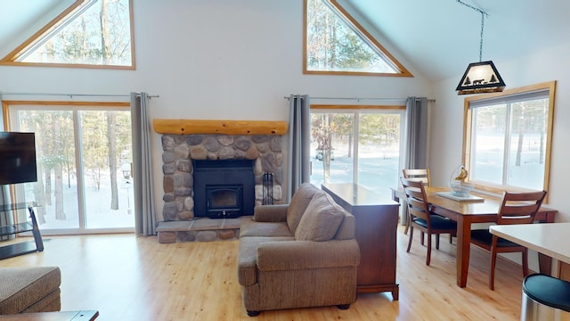 living room featuring high vaulted ceiling, a wood stove, light hardwood / wood-style flooring, and a healthy amount of sunlight