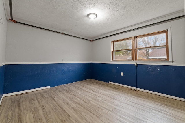 empty room featuring a textured ceiling, light hardwood / wood-style floors, and ornamental molding