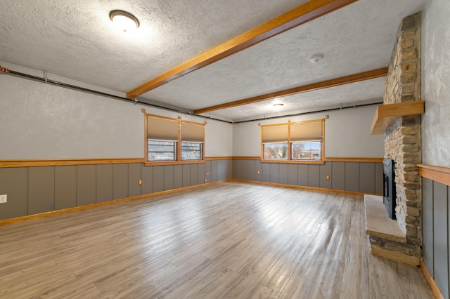 unfurnished living room with beamed ceiling, a stone fireplace, light wood-type flooring, and a textured ceiling