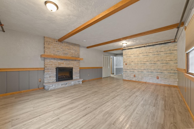 unfurnished living room with beam ceiling, a fireplace, a textured ceiling, and light wood-type flooring