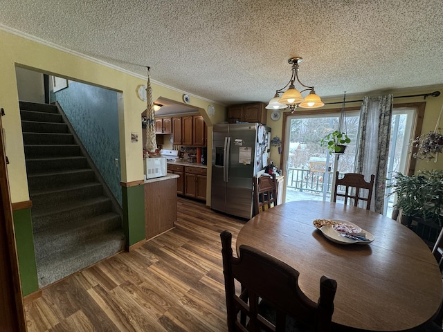 dining area with a textured ceiling, dark hardwood / wood-style flooring, crown molding, and a chandelier