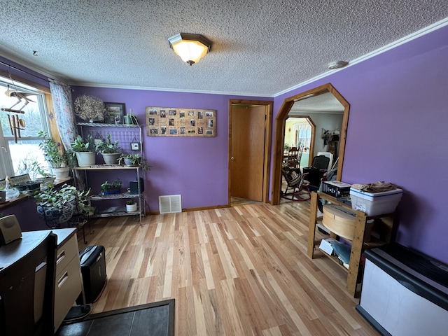 interior space with a textured ceiling, ornamental molding, and light wood-type flooring