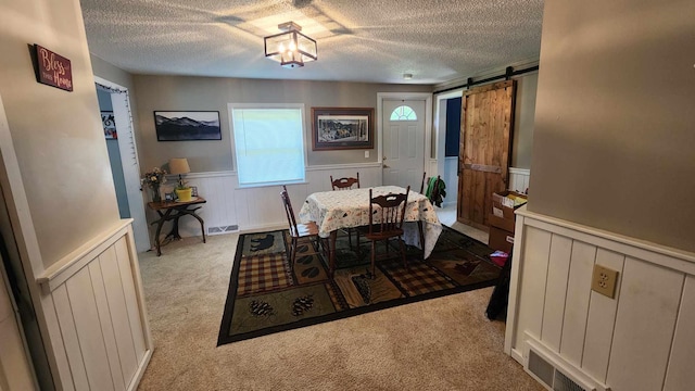 carpeted dining room with a textured ceiling and a barn door