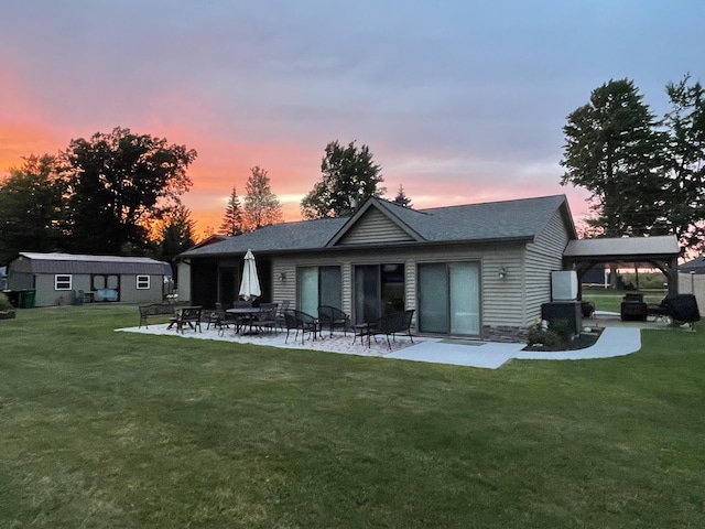 back house at dusk with a patio area, a lawn, and an outdoor structure