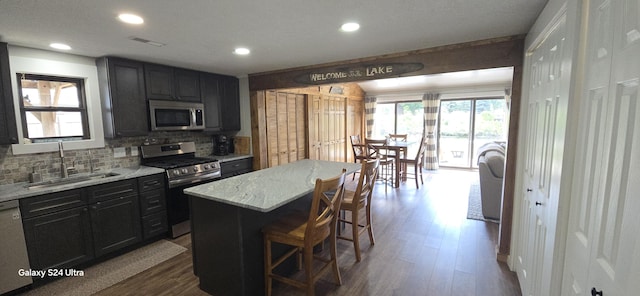 kitchen with stainless steel appliances, sink, a center island, light stone counters, and a kitchen bar