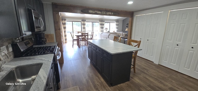 kitchen with a breakfast bar area, appliances with stainless steel finishes, dark hardwood / wood-style flooring, a kitchen island, and sink