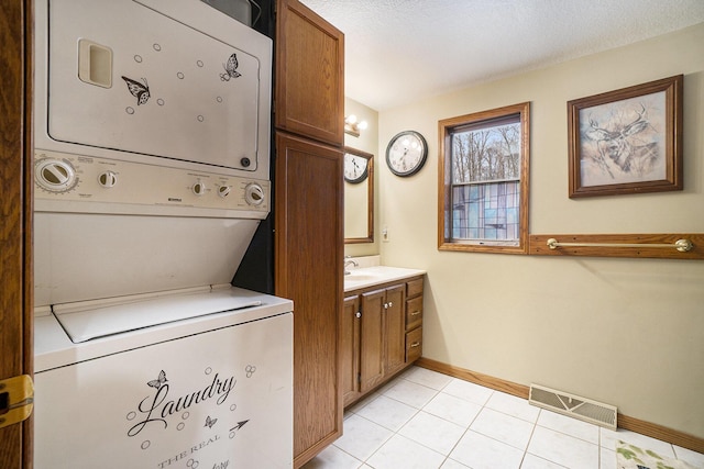 laundry area with sink, a textured ceiling, cabinets, light tile patterned flooring, and stacked washer / drying machine