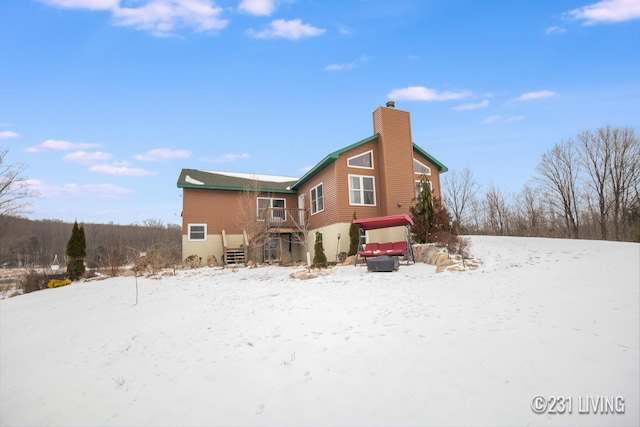 snow covered rear of property with a wooden deck and a hot tub