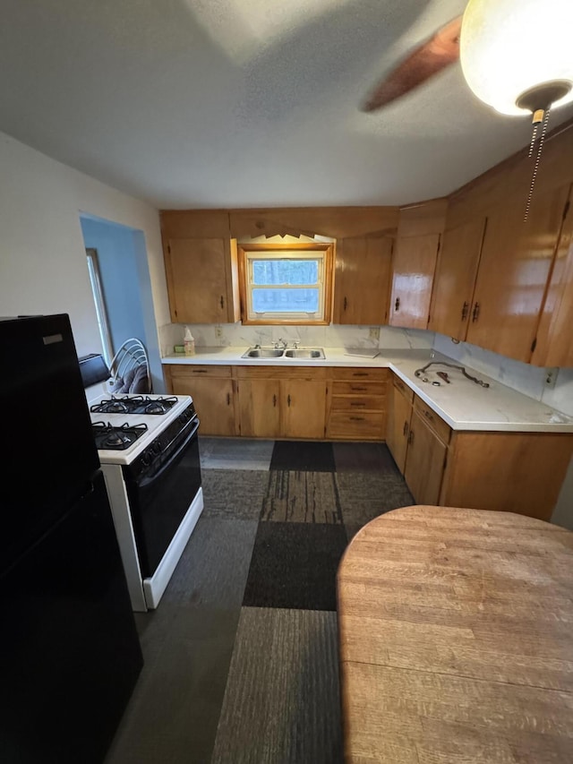 kitchen featuring range with gas stovetop, black refrigerator, decorative backsplash, sink, and ceiling fan