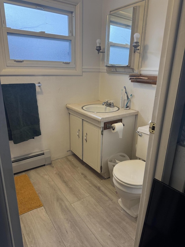 bathroom with hardwood / wood-style floors, a wealth of natural light, a baseboard heating unit, vanity, and toilet