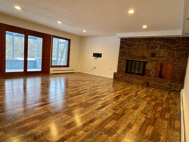 unfurnished living room featuring a textured ceiling, baseboard heating, dark hardwood / wood-style floors, and a stone fireplace