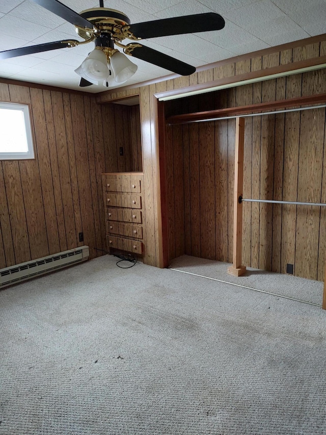 basement with ceiling fan, a baseboard radiator, wood walls, and carpet flooring