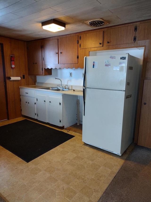 kitchen featuring white fridge, wooden walls, and sink