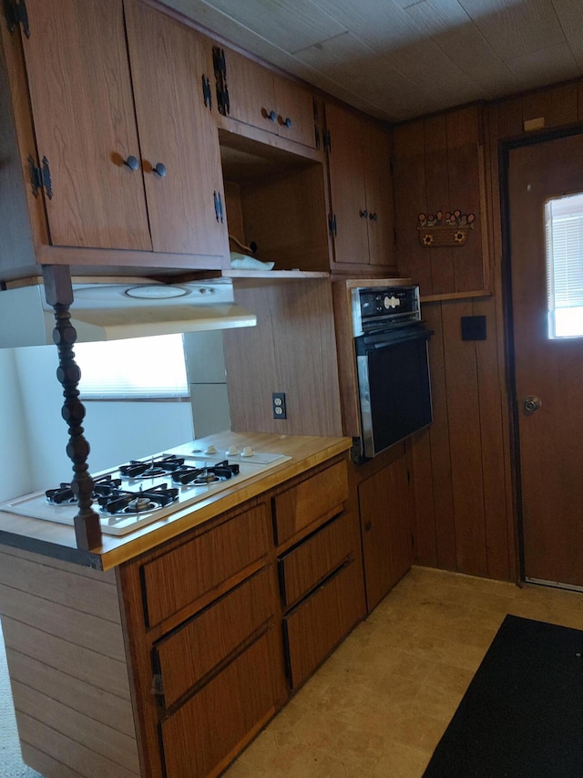 kitchen featuring white gas cooktop, kitchen peninsula, oven, and wooden walls