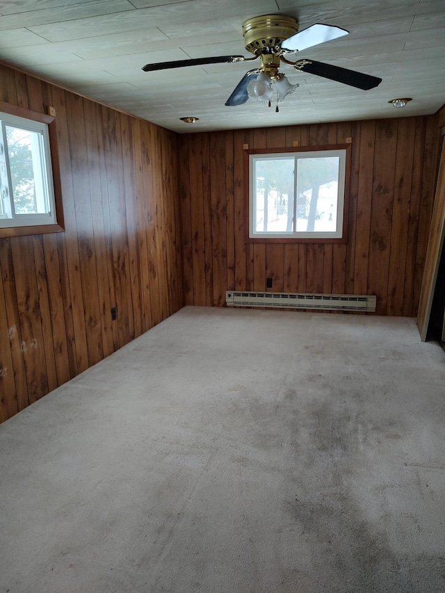 carpeted empty room featuring ceiling fan, a baseboard radiator, plenty of natural light, and wooden walls