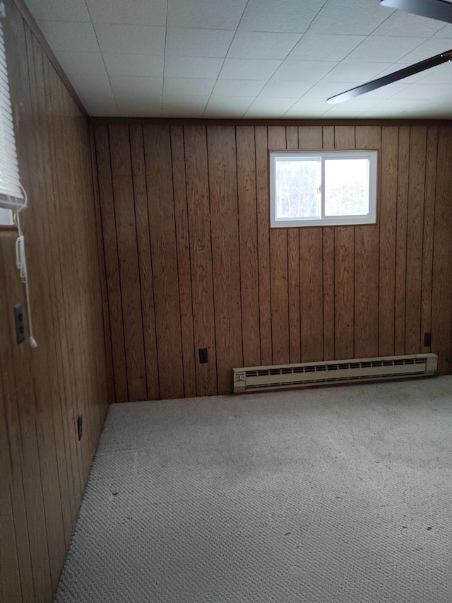 basement with baseboard heating, wooden walls, and carpet flooring