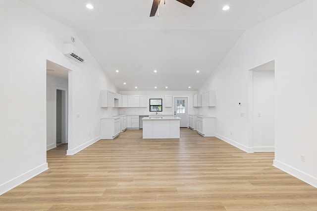 kitchen with light wood finished floors, baseboards, white cabinets, a kitchen island, and open floor plan