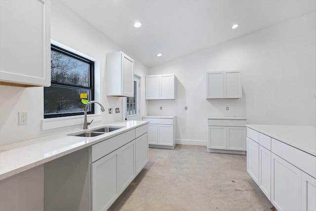 kitchen with light stone counters, sink, white cabinets, and lofted ceiling