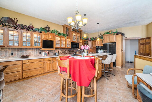 kitchen featuring sink, backsplash, hanging light fixtures, a kitchen island with sink, and black appliances