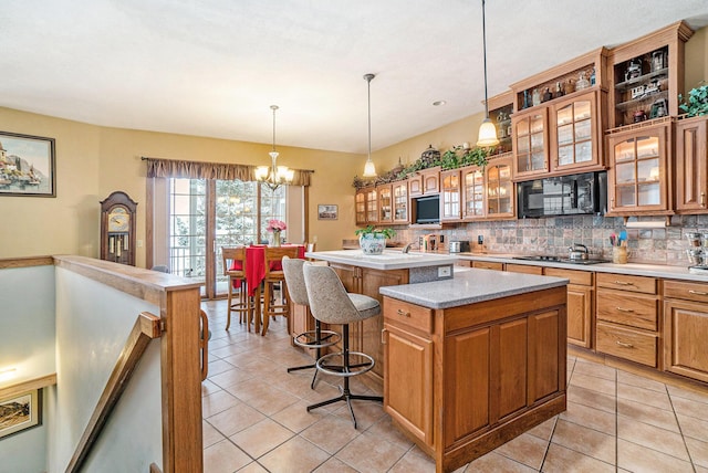 kitchen with a breakfast bar, a center island, hanging light fixtures, light tile patterned floors, and black appliances