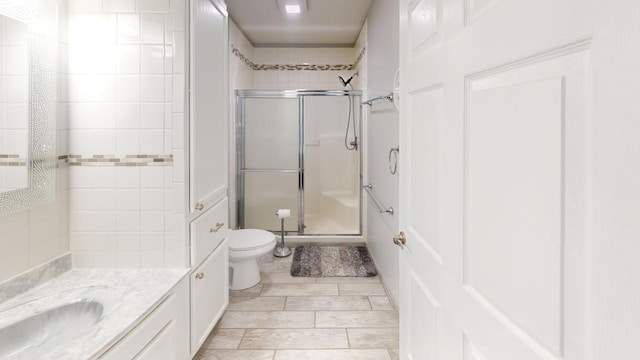 bathroom featuring toilet, vanity, and a shower with shower door