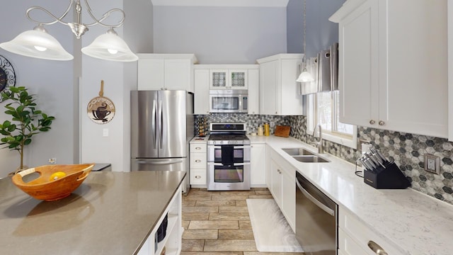 kitchen featuring sink, hanging light fixtures, appliances with stainless steel finishes, decorative backsplash, and white cabinets