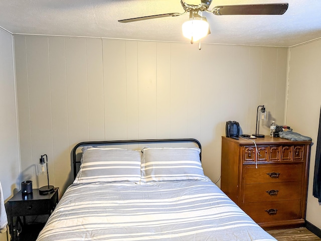 bedroom with a textured ceiling, wooden walls, and ceiling fan