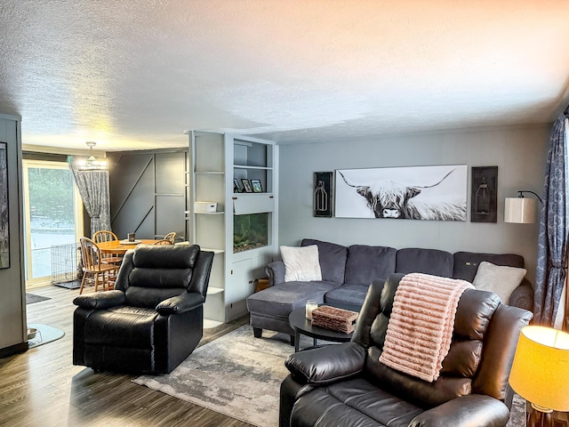 living room with built in shelves, wood-type flooring, and a textured ceiling